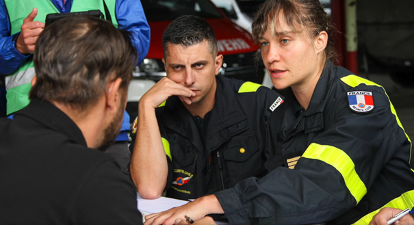 Three emergency response personnel are in a group. They are in uniform and are talking intently.