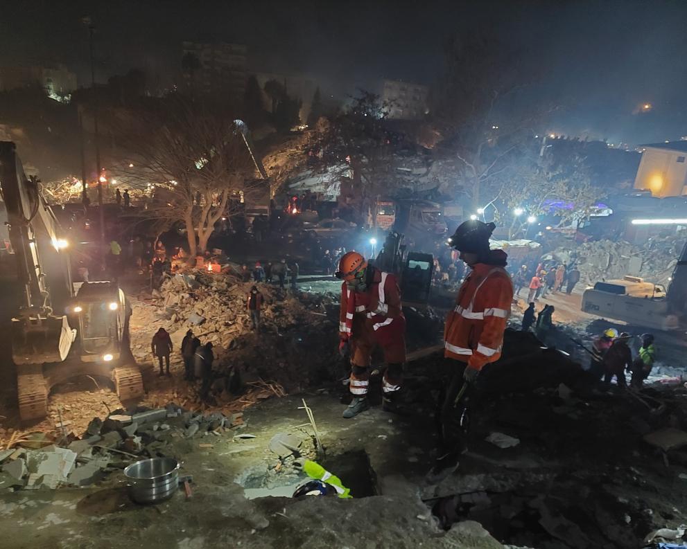 Rescuers search the ruined city by night under floodlights