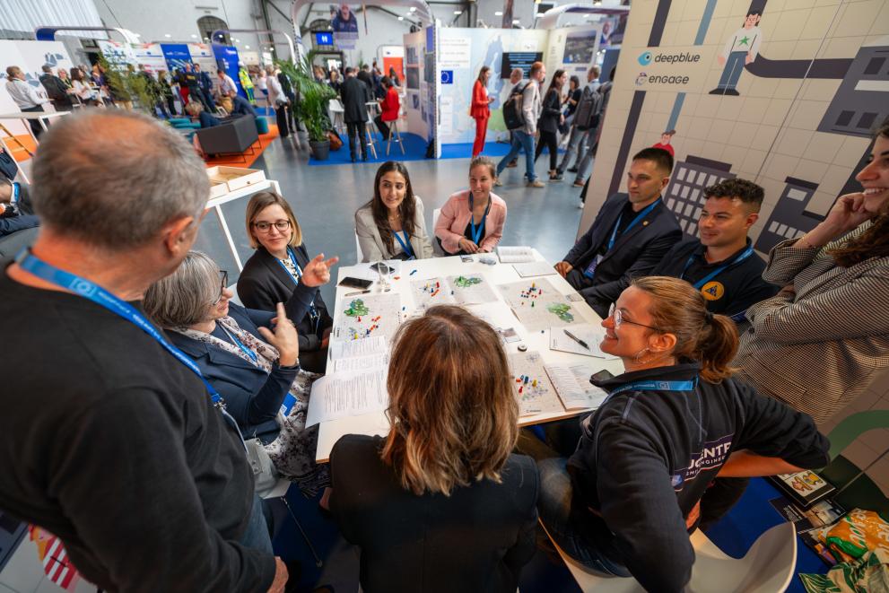 Group of people sitting around a table with maps, at a conference setting.