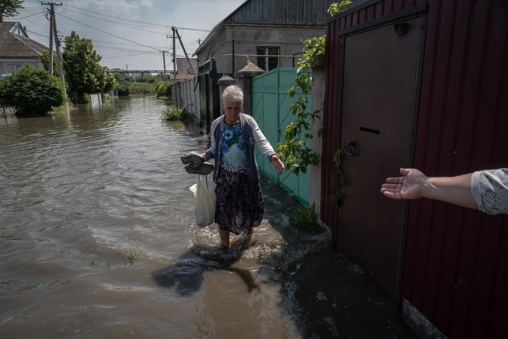 Person reaching out to an elderly woman in a flooded street.