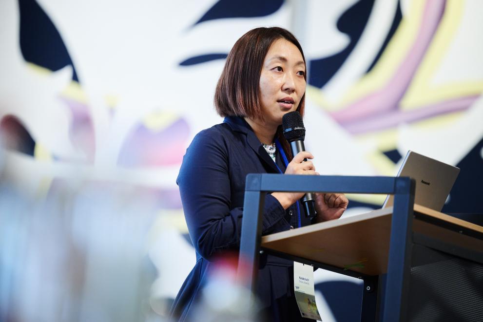 Professor Kanako Iuchi on stage, holding a microphone while delivering her speech.