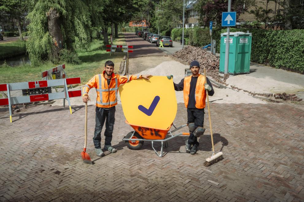 Two road workers hold the shield of the think ahead campaign during their work