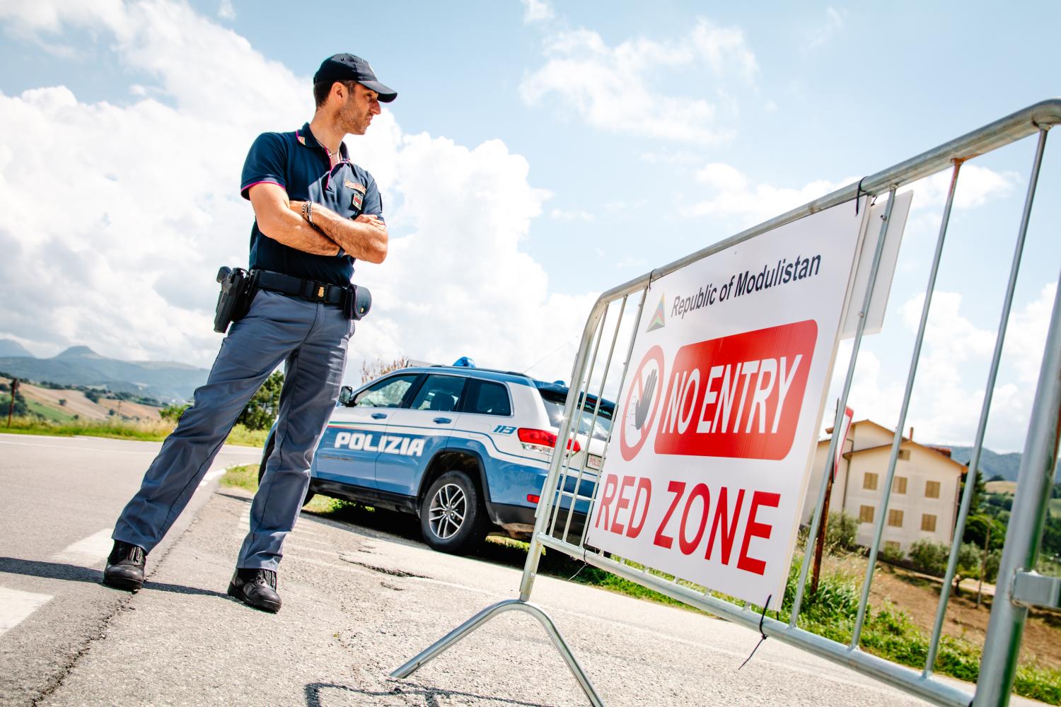 A security officer stands behind a barrier. On the barrier there is a sign which reads 'No Entry. Red Zone.'