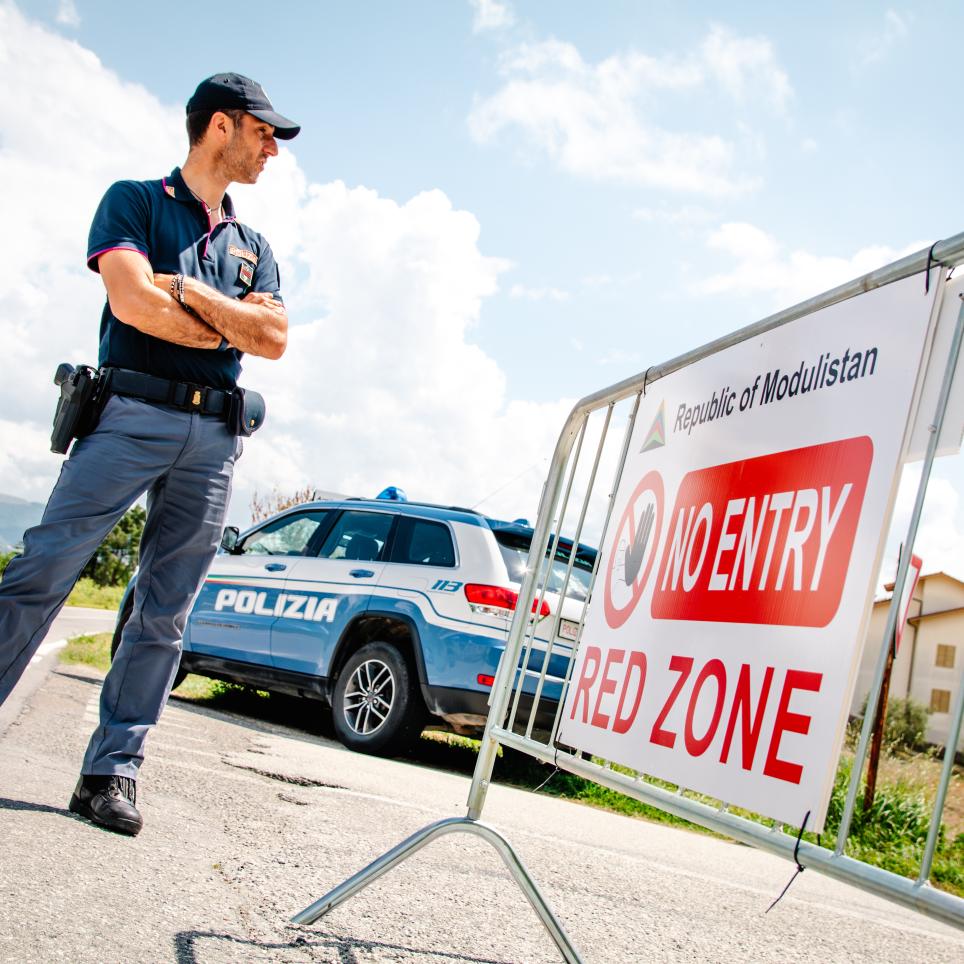 A security officer stands behind a barrier. On the barrier there is a sign which reads 'No Entry. Red Zone.'