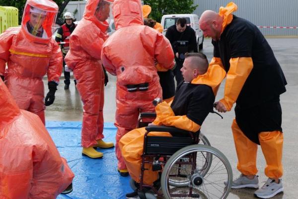 A wheelchair user is escorted to a disinfection station during a CBRN exercise.