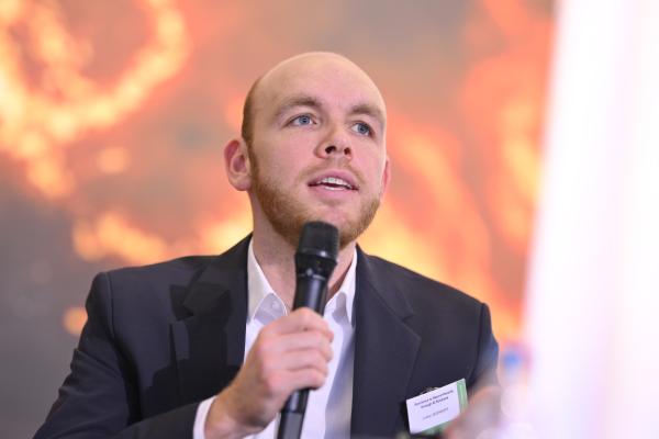 Lukas Liesenhoff, seated, with microphone in hand, with a backdrop which depicts flames