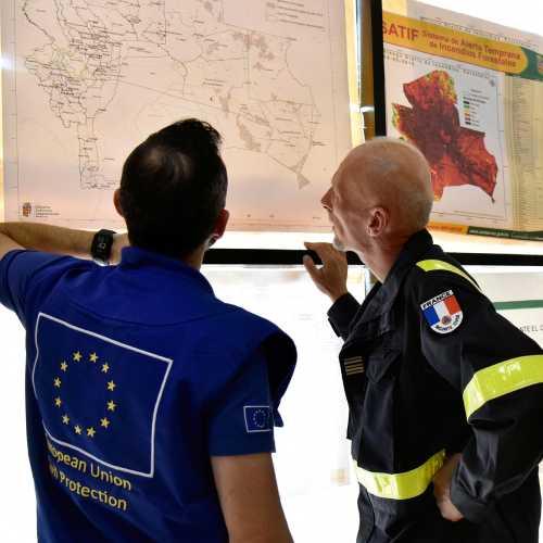 Two civil protection personnel looking at and discussing a map put up on a wall
