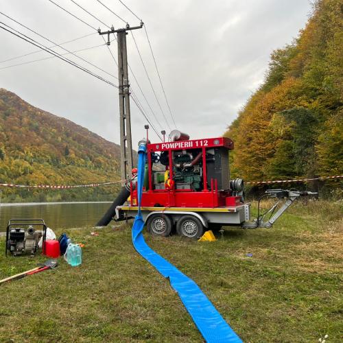 A red high-capacity water pumping machine marked ‘Pompieri’ is positioned at the edge of a reservoir, ready to start pumping