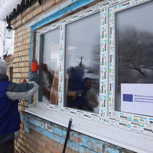 A worker installs a window frame in a house in Ukraine. There is snow on the ground.