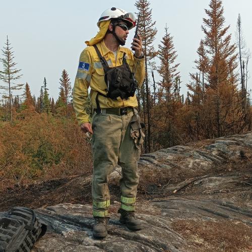 A firefighter in protective clothing speaks into a communication device