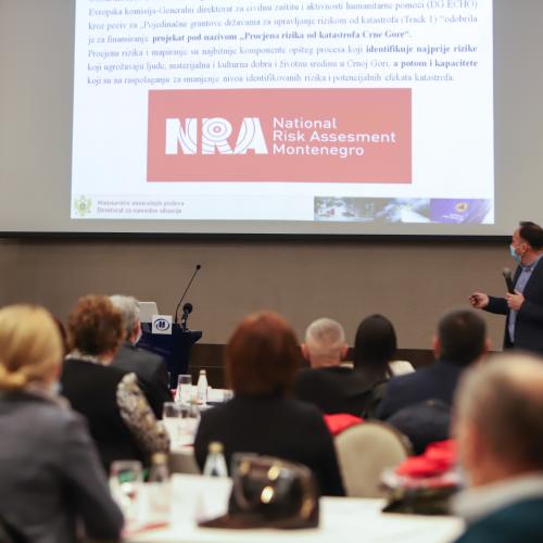 Room full of people watching a presentation and a white screen with text and a red logo reading 'National Risk Assessment Montenegro'.