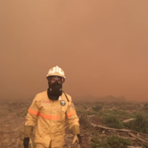 Marco Pires in his protective suit on burnt terrain in proximity of a wildfire.