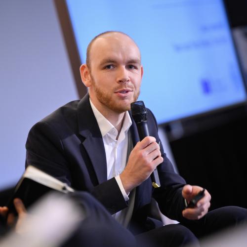 Lukas Liesenhoff during his speech, seated, with a microphone in his hand, looking directly into the camera.