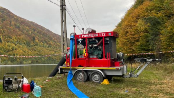 A red high-capacity water pumping machine marked ‘Pompieri’ is positioned at the edge of a reservoir, ready to start pumping