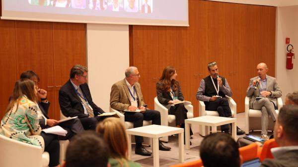 Man speaking during break out session. He is seated next to six other panel members.