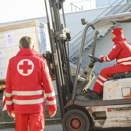 Red Cross personnel with a forklift loading a pallet with boxes on a truck