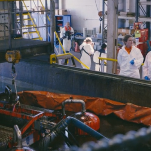 Two people talking, next to a oil skimmer in a pool. The picture is taken in NCAs testing facilities.