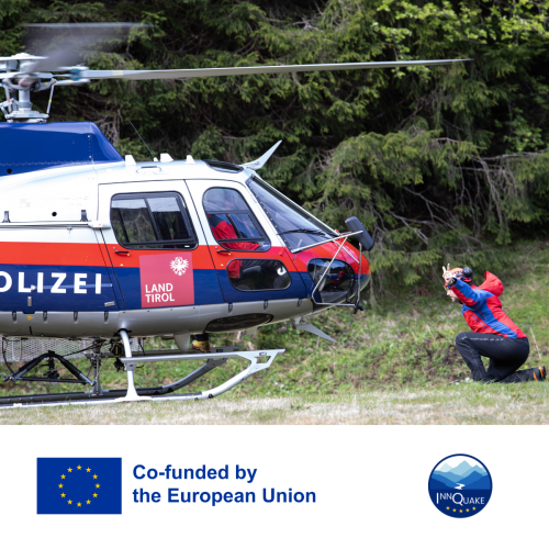 A helicopter landing on grass, a person in front of it instructing the pilot. 