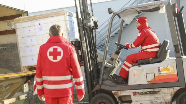 Red Cross personnel with a forklift loading a pallet with boxes on a truck
