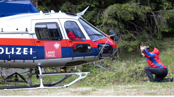 A helicopter landing on grass, a person in front of it instructing the pilot. 